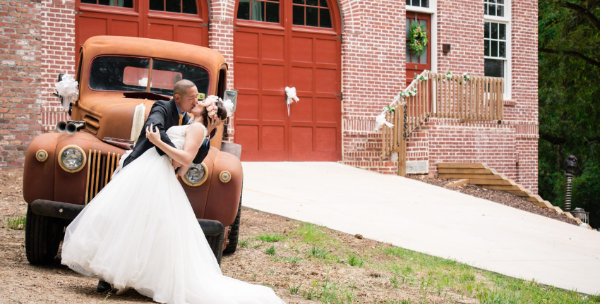 Couple kissing with an old car and Old Smyrna Firehouse in the background